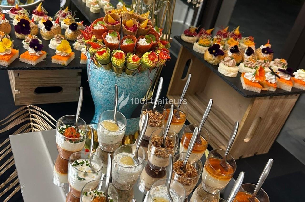 Buffet de verrines, canapés et amuse-bouches colorés, décorés de fleurs comestibles, présentés sur des plateaux élégants.