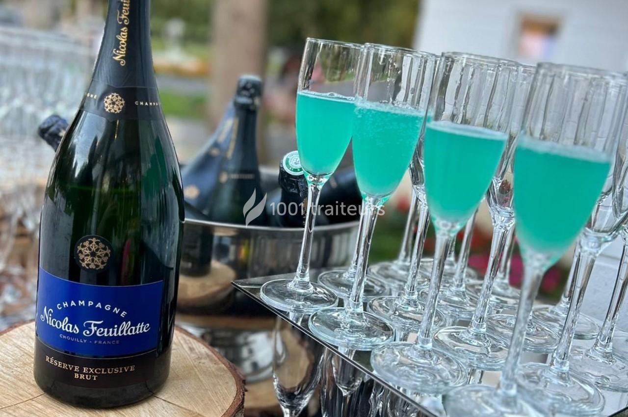 Bouteille de champagne et flûtes remplies d'un cocktail bleu, disposées sur une table en extérieur.