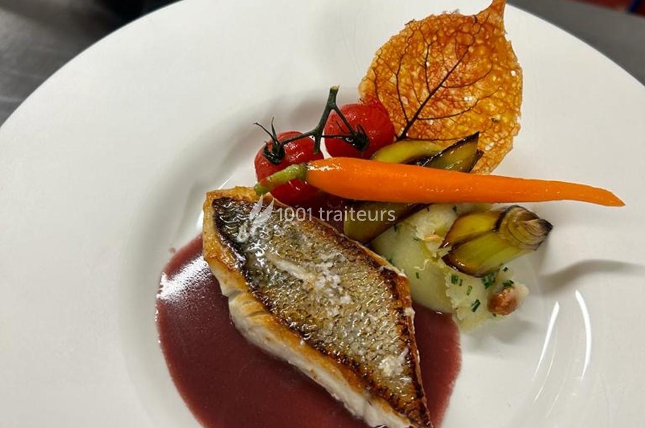 Filet de poisson grillé avec sauce rouge, légumes rôtis, carotte entière et chips de feuille sur une assiette blanche.