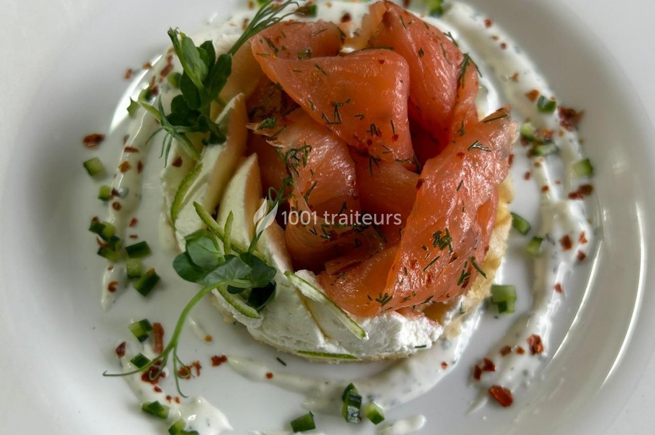 Tranches de saumon fumé disposées sur un lit de fromage frais, accompagnées de concombres et herbes fraîches.