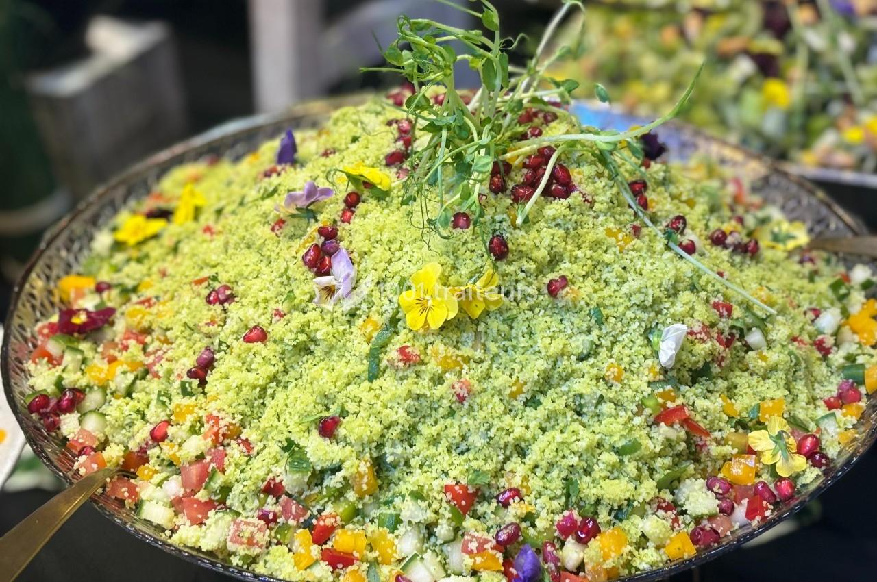 Plat de taboulé coloré garni de grenade, fleurs comestibles et herbes fraîches, présenté dans un grand plat.