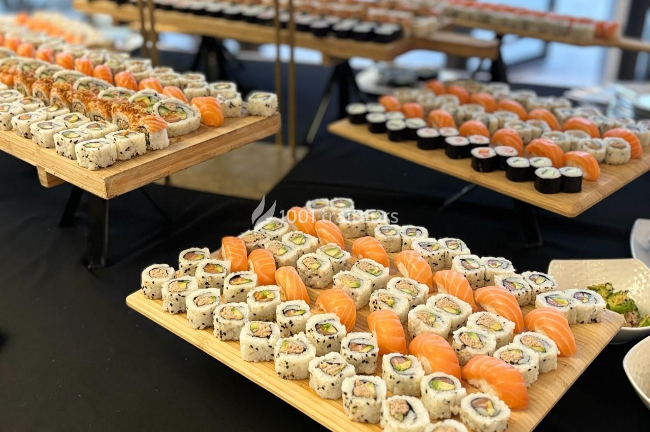 Plateaux de sushis variés disposés sur des tables, comprenant makis, nigiris et autres assortiments.