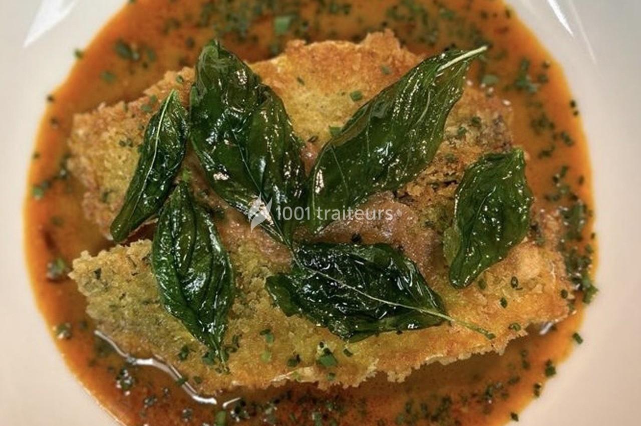 Plat de poisson pané garni de feuilles de basilic frit, servi dans une sauce tomate avec des herbes hachées.