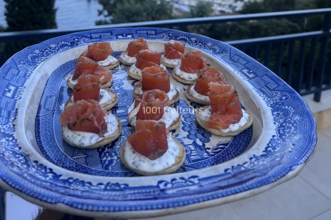 Plateau de canapés au saumon fumé et crème sur un plat en porcelaine bleue, présenté en extérieur.