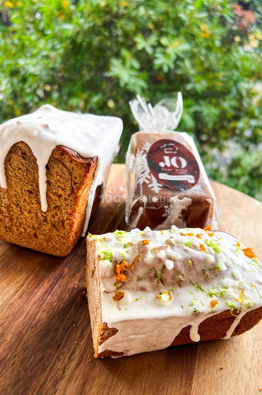 Trois cakes glacés, dont un tranché, posés sur une planche en bois devant un fond de verdure.