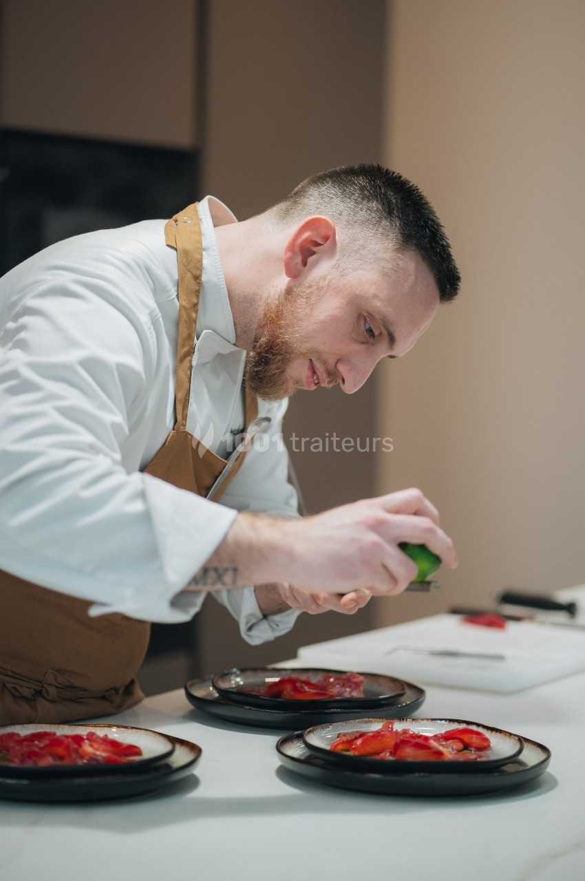 Un chef en tablier prépare des assiettes avec soin, ajoutant une touche finale à un plat coloré.