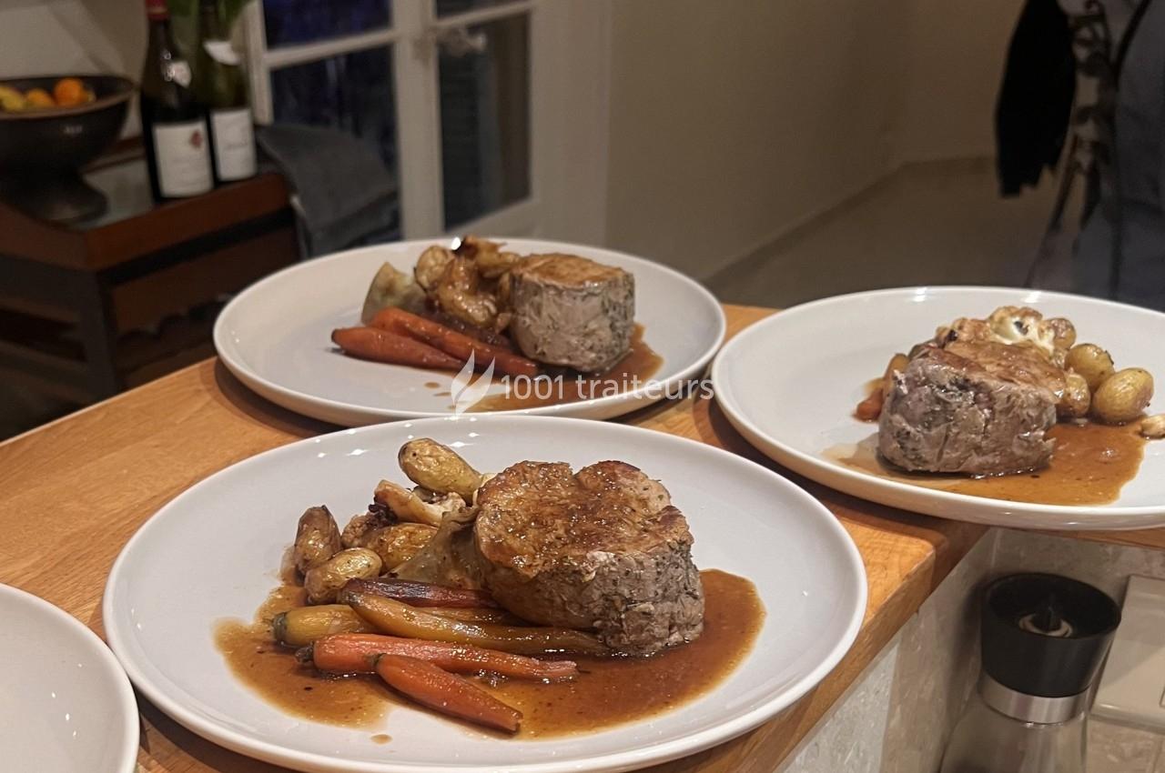 Assiettes de filet de viande servi avec carottes, pommes de terre rôties et sauce, disposées sur un comptoir en bois.