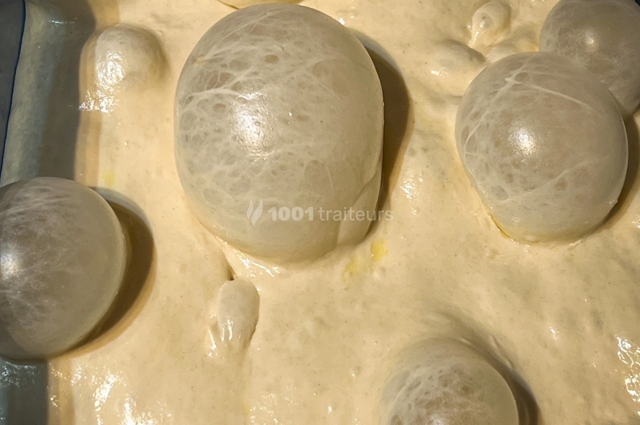 Bulles translucides gonflées à la surface d'une pâte beige dans un récipient rectangulaire.