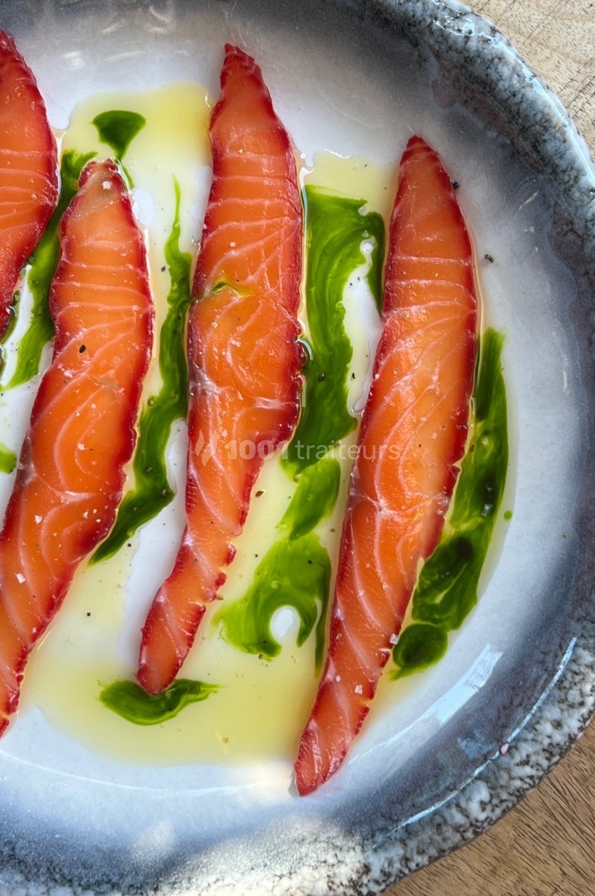 Tranches de saumon cru marinées, disposées avec de l'huile et une sauce verte sur une assiette en céramique.