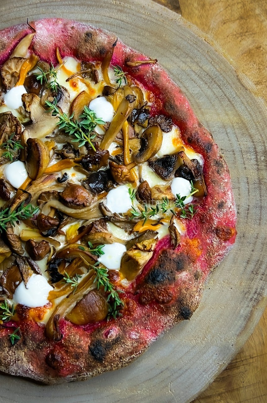 Pizza garnie de champignons, de fromage, de crème et de brins de thym, servie sur une planche en bois.