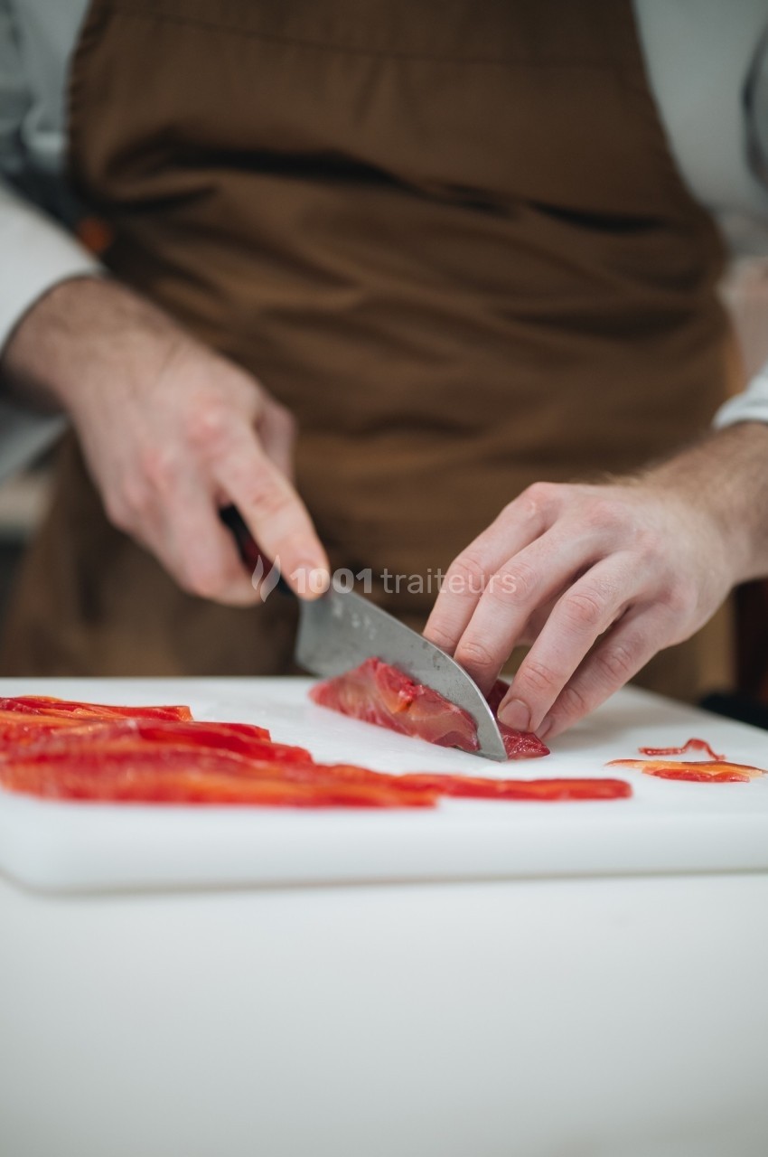 Un cuisinier découpe des poivrons rouges sur une planche blanche avec un couteau.
