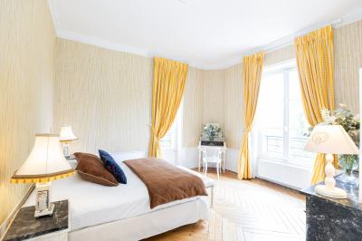 Chambre lumineuse avec lit double, parquet, rideaux orange, lustre et grandes fenêtres donnant sur l'extérieur.