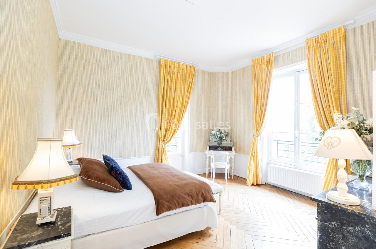 Chambre lumineuse avec lit double, parquet en bois, rideaux jaunes et bureau près d'une fenêtre.