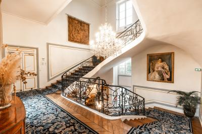 Chambre lumineuse avec lit double, parquet, rideaux orange, lustre et grandes fenêtres donnant sur l'extérieur.