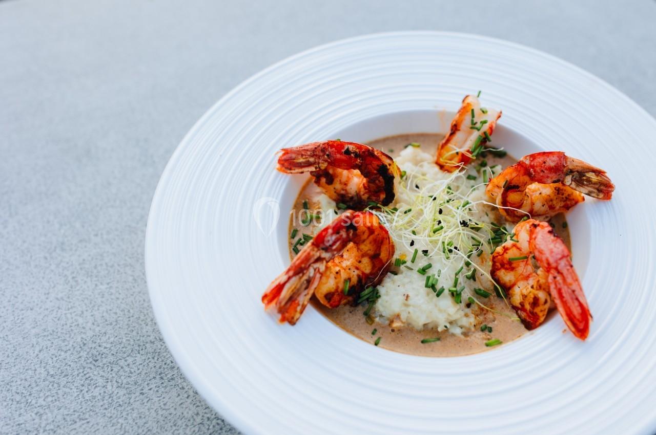 Assiette de crevettes grillées servies sur une purée avec une sauce et des pousses fraîches en garniture.