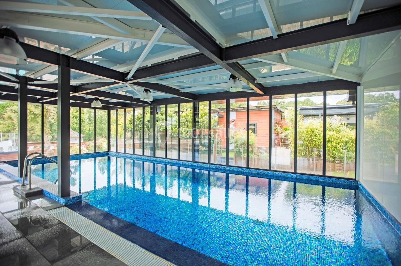 Piscine intérieure avec carrelage bleu, entourée de grandes baies vitrées donnant sur un jardin verdoyant.