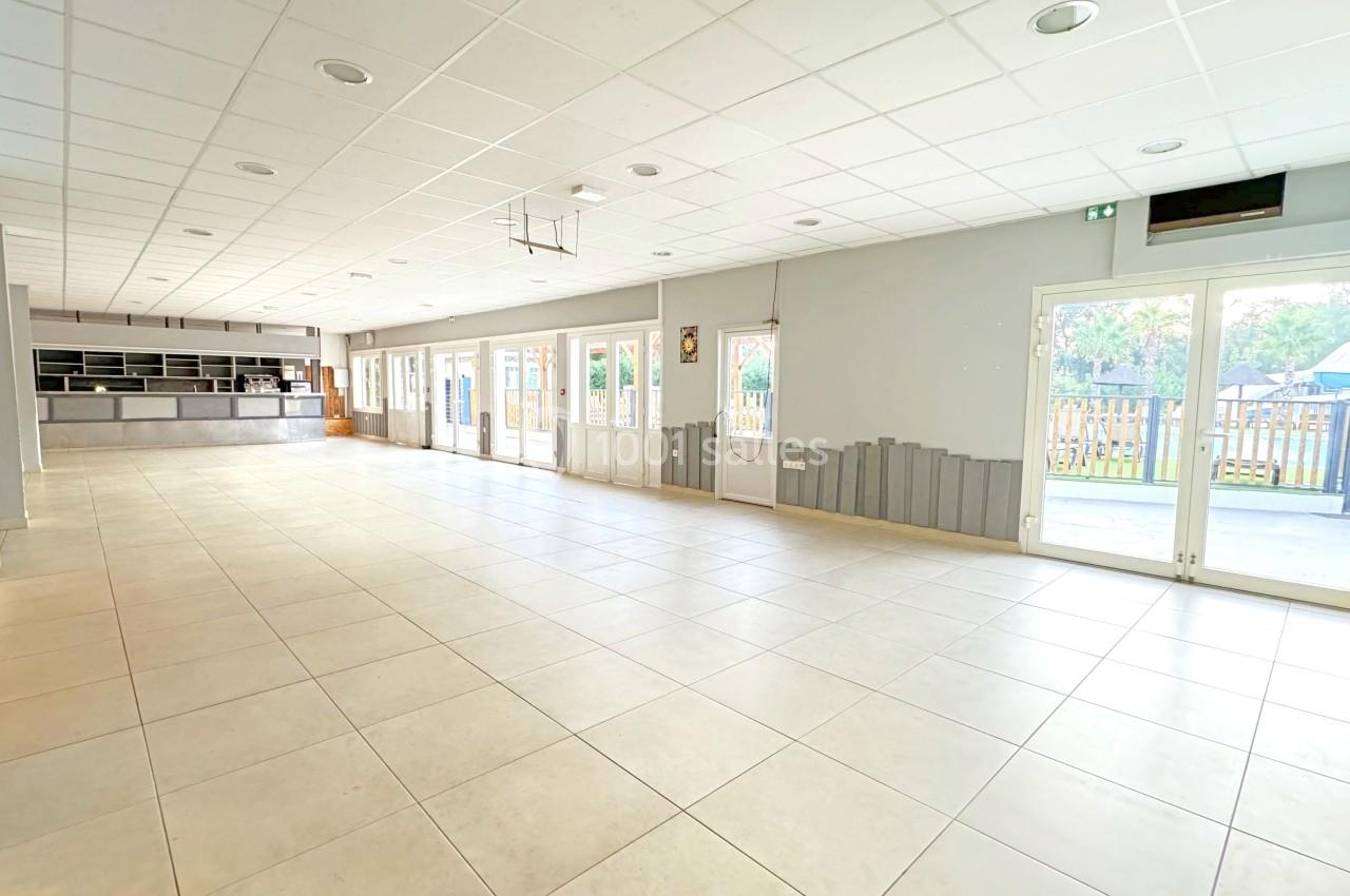 Salle lumineuse avec carrelage clair, grandes baies vitrées, comptoir au fond et vue sur un espace extérieur.