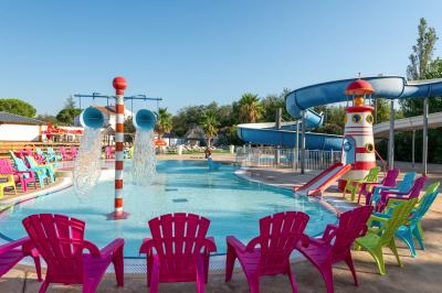 Un enfant avec des brassards orange glisse sur un toboggan rouge dans une piscine extérieure ensoleillée.