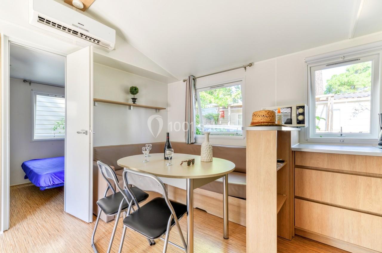 Intérieur d'un petit logement avec coin repas, table ronde, chaises, étagères, et chambre visible à travers une porte…