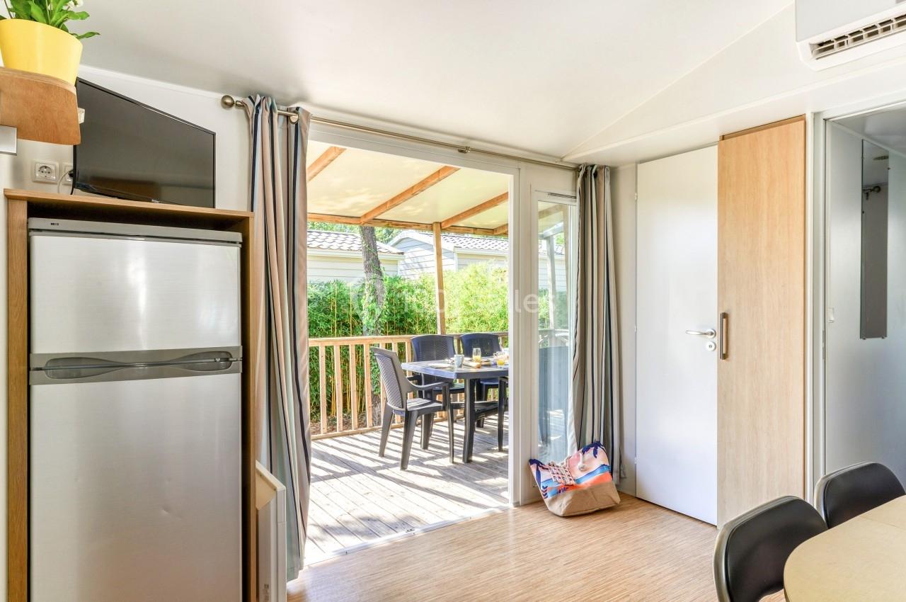 Intérieur lumineux avec vue sur une terrasse en bois aménagée, table et chaises extérieures visibles à travers une baie…