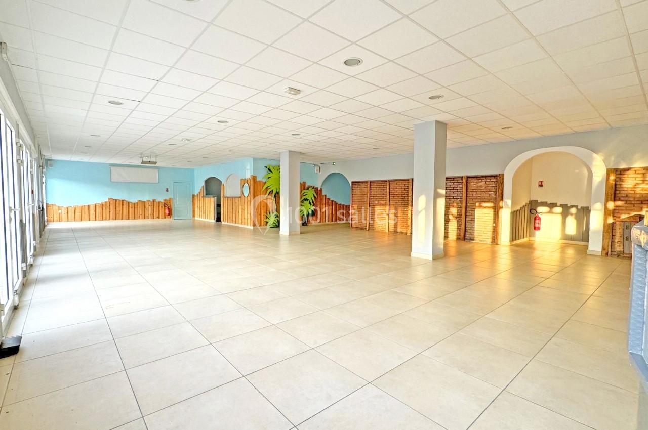 Salle spacieuse et lumineuse avec carrelage clair, murs décorés et grandes fenêtres laissant entrer la lumière naturelle.