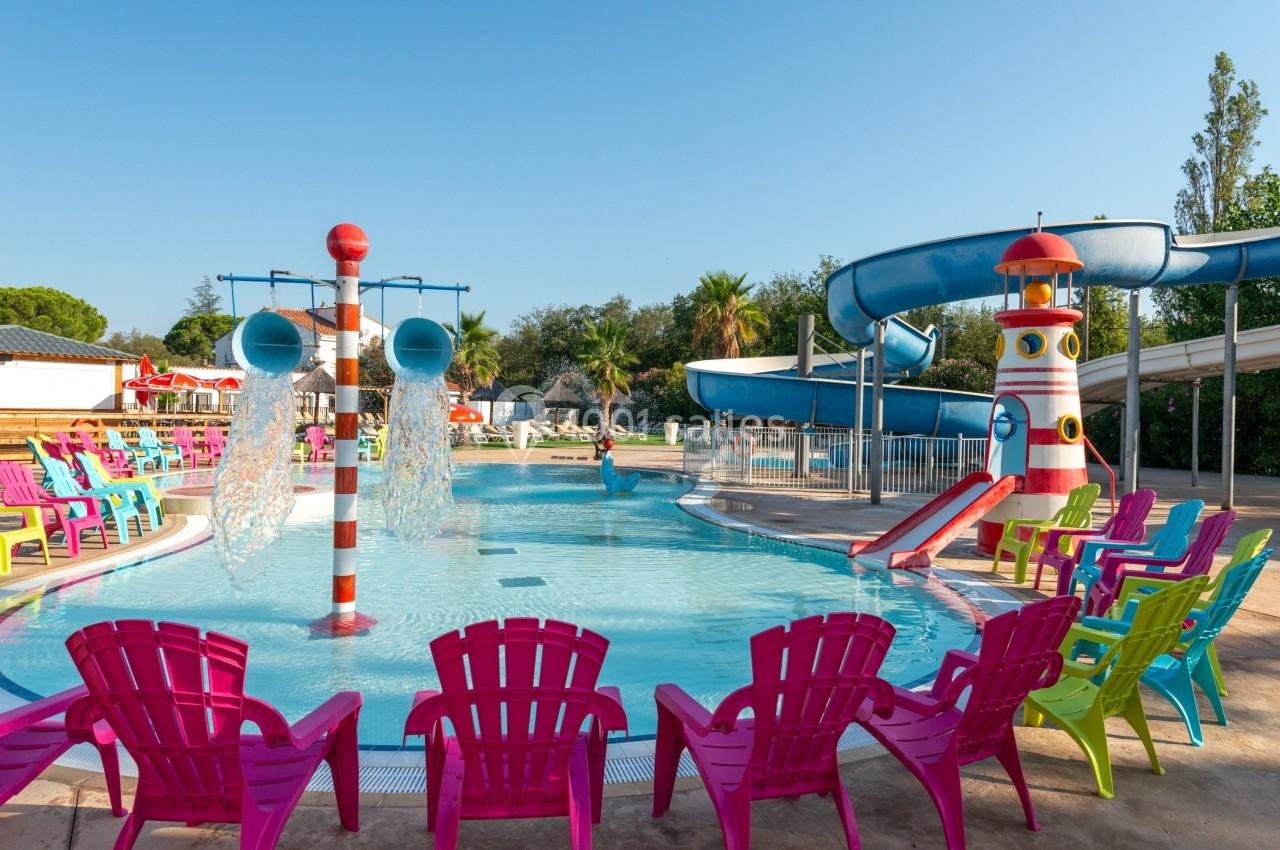 Piscine extérieure avec toboggans, jets d'eau et chaises colorées disposées autour sous un ciel dégagé.
