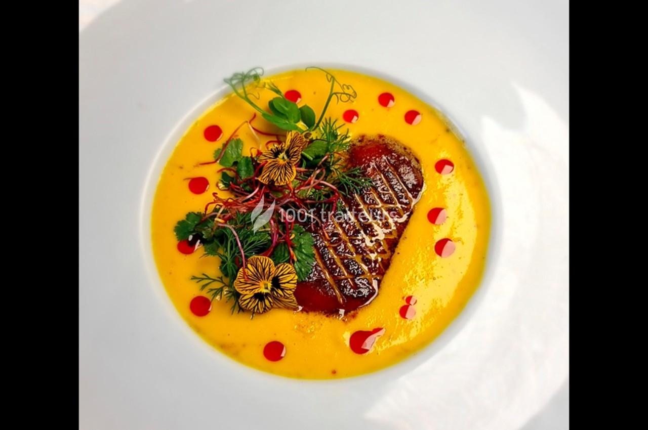 Plat gastronomique composé d'un morceau de viande grillée, sauce jaune, herbes fraîches et fleurs comestibles.