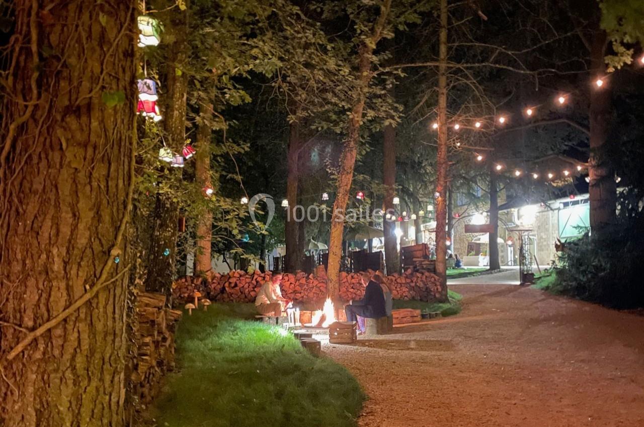 Un groupe de personnes assises autour d'un feu de camp dans une forêt éclairée par des guirlandes lumineuses.