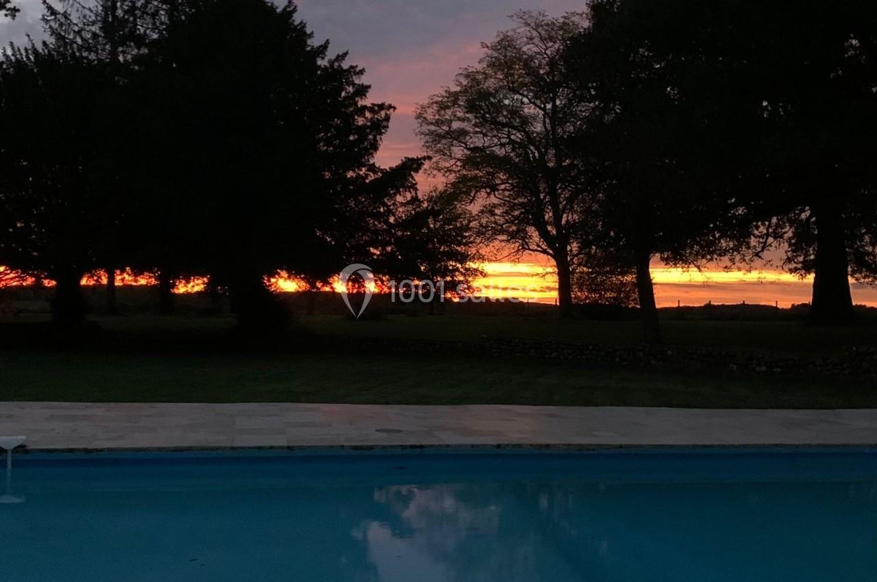 Piscine extérieure au crépuscule, reflétant un ciel coloré avec des arbres en arrière-plan.