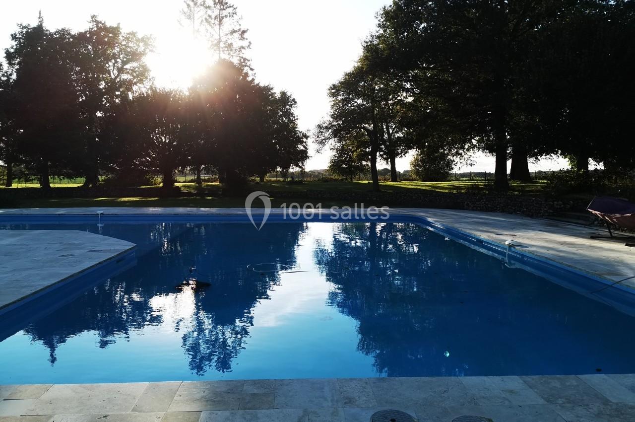 Piscine extérieure entourée d'arbres avec le soleil couchant reflété dans l'eau calme.