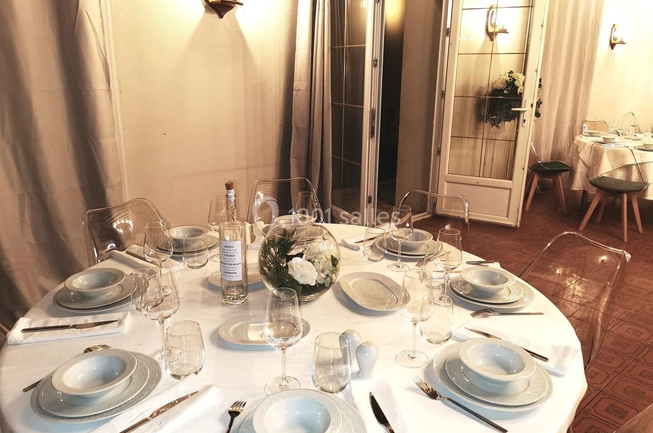 Table ronde dressée avec vaisselle blanche, verres et décoration florale, dans une salle lumineuse aux tons neutres.