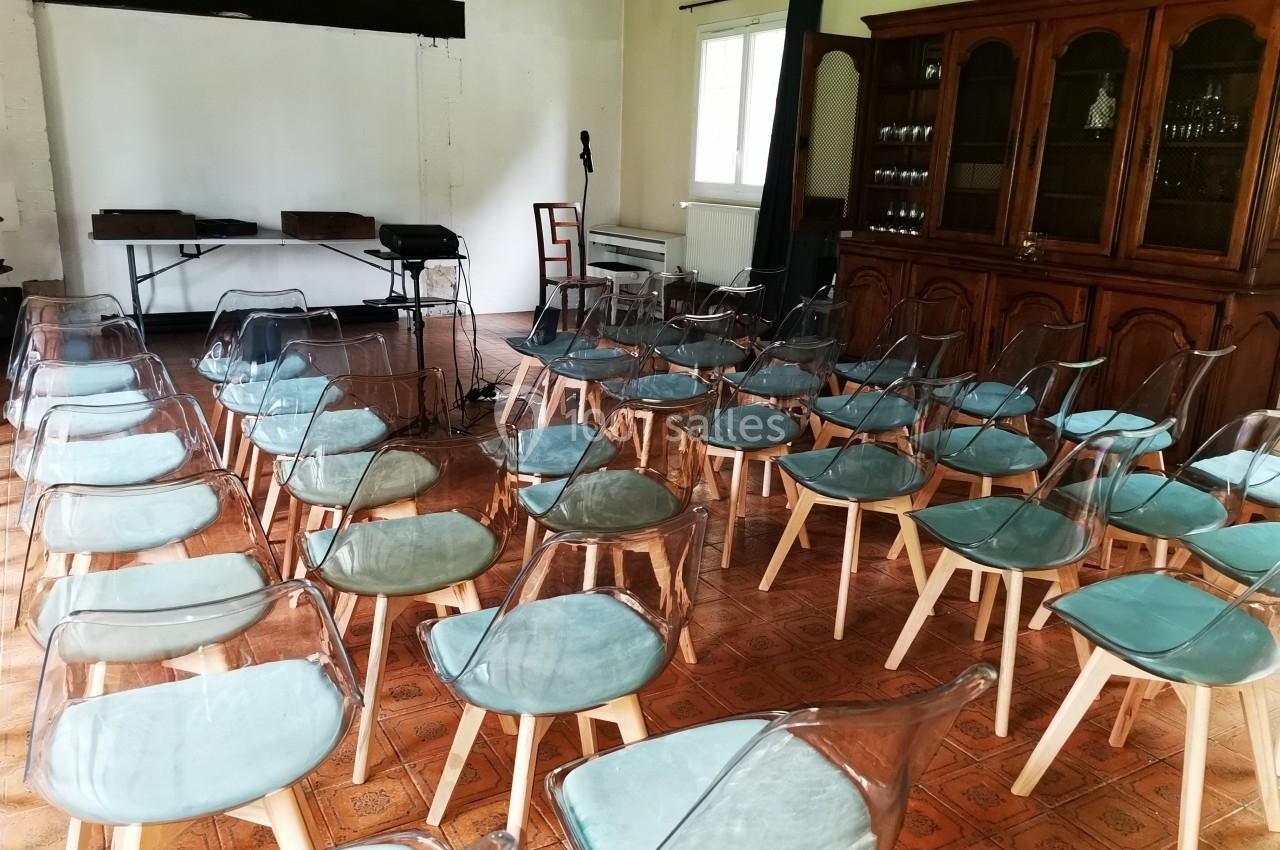 Salle aménagée avec des chaises transparentes et coussins bleus, face à un écran blanc et un micro sur pied.