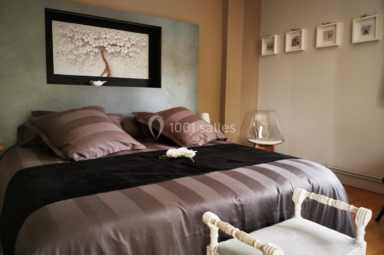Lit double avec couvre-lit gris, coussins assortis, tableau floral en tête de lit et décoration minimaliste.