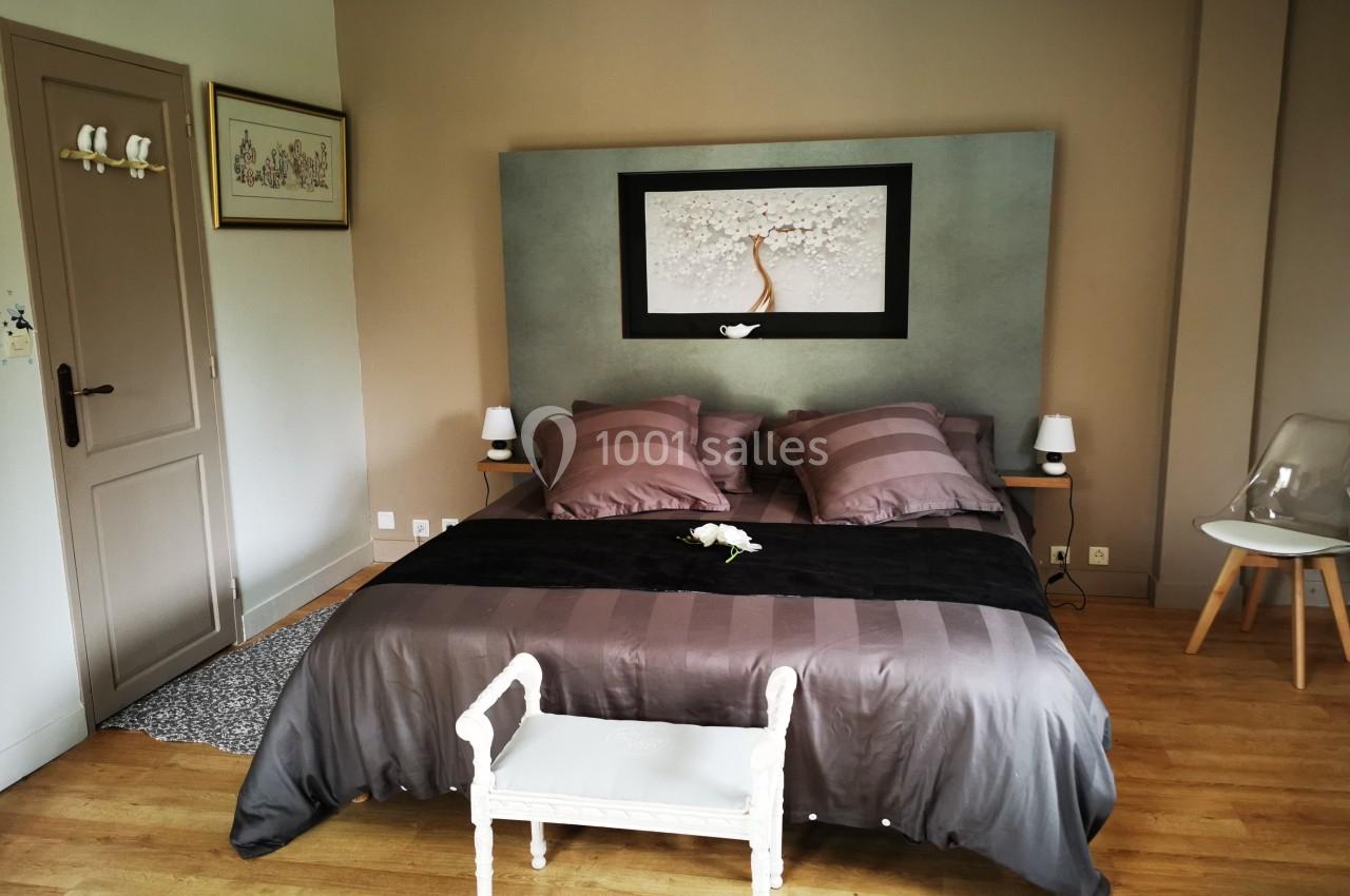 Chambre avec lit double, tête de lit décorée, murs beige, parquet au sol et mobilier minimaliste.