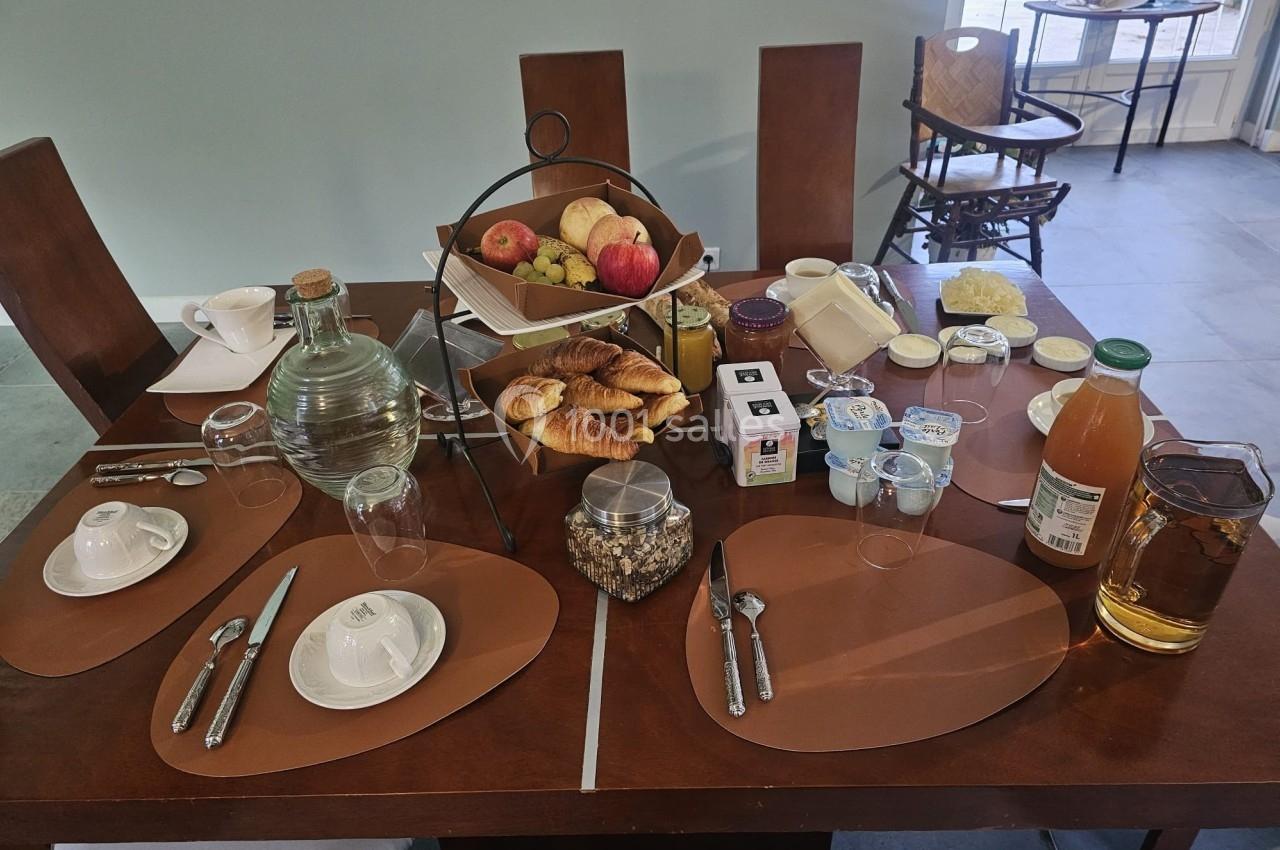 Table dressée pour le petit-déjeuner avec viennoiseries, fruits, jus, confitures, yaourts et boissons chaudes.