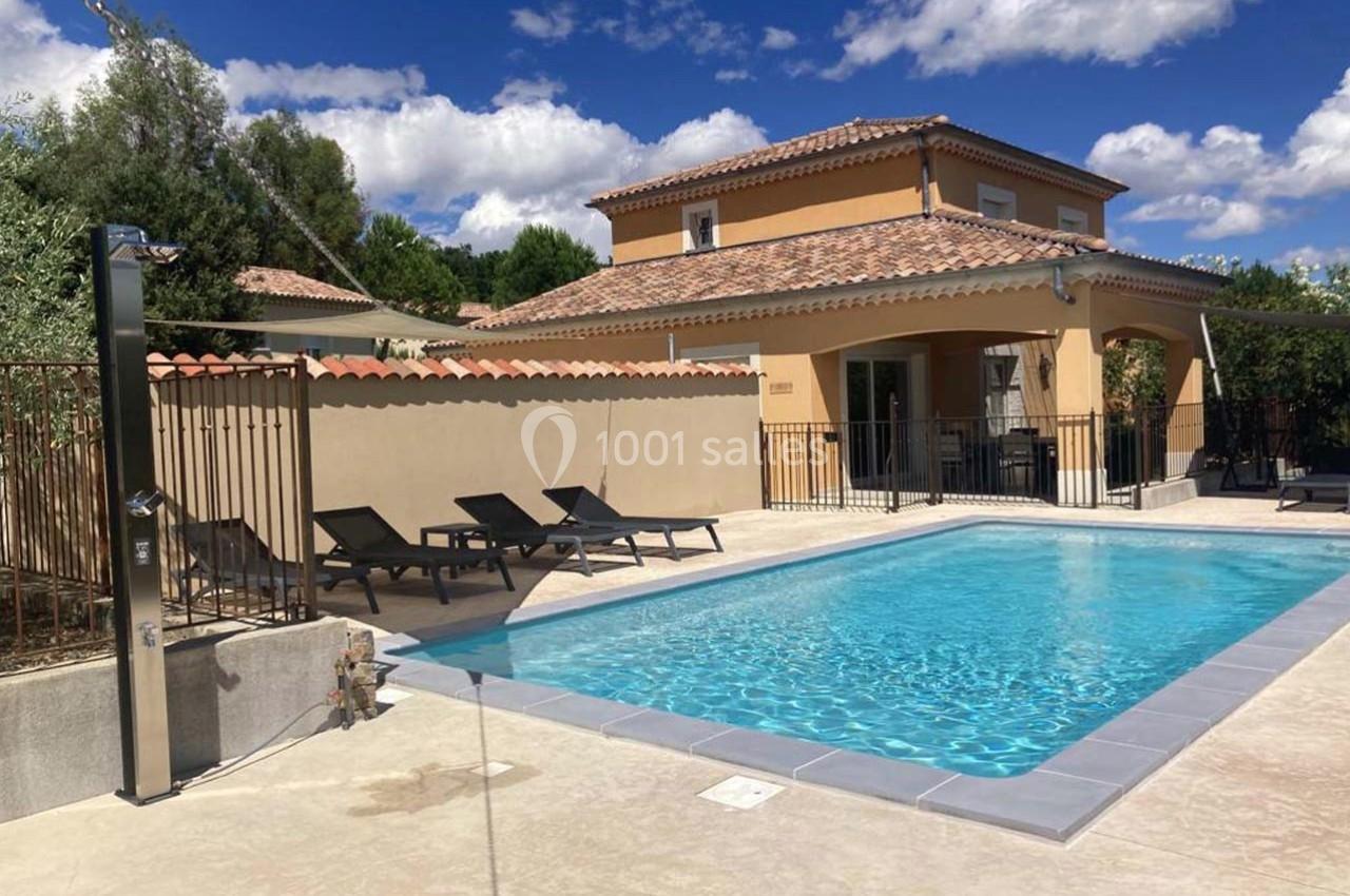 Maison avec piscine extérieure, terrasse aménagée de transats, douche solaire et ciel dégagé en arrière-plan.