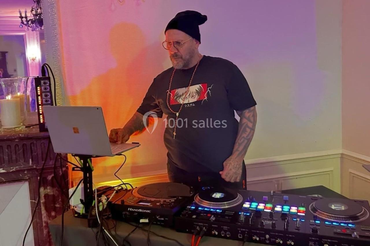Un DJ portant un bonnet mixe de la musique sur une console, avec un ordinateur portable à ses côtés dans une pièce éclairée.