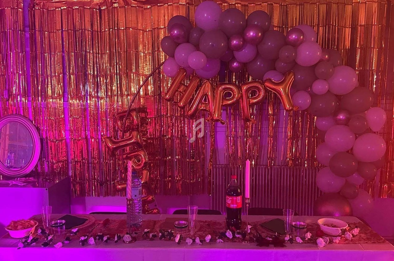 Décoration de fête avec ballons, guirlandes dorées, table dressée avec boissons, bougies et collations.