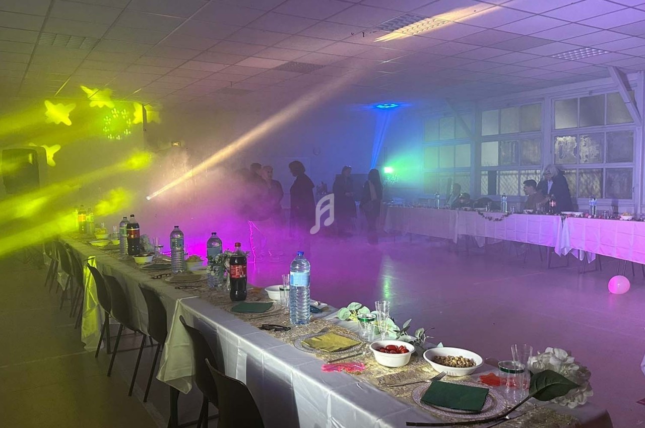 Salle de réception décorée avec des tables dressées, éclairages colorés et fumée créant une ambiance festive.