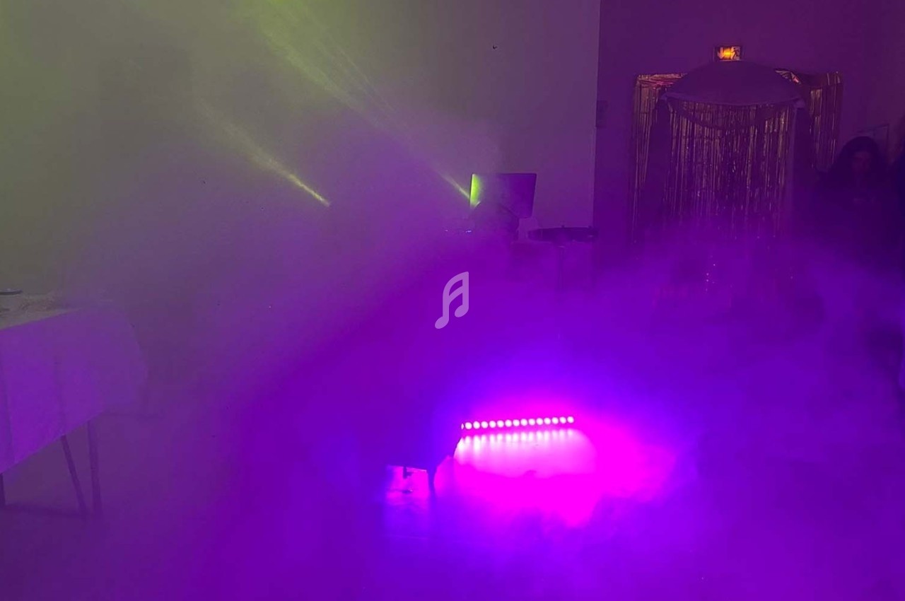 Salle plongée dans une ambiance lumineuse violette et verte avec des faisceaux lumineux et de la fumée.