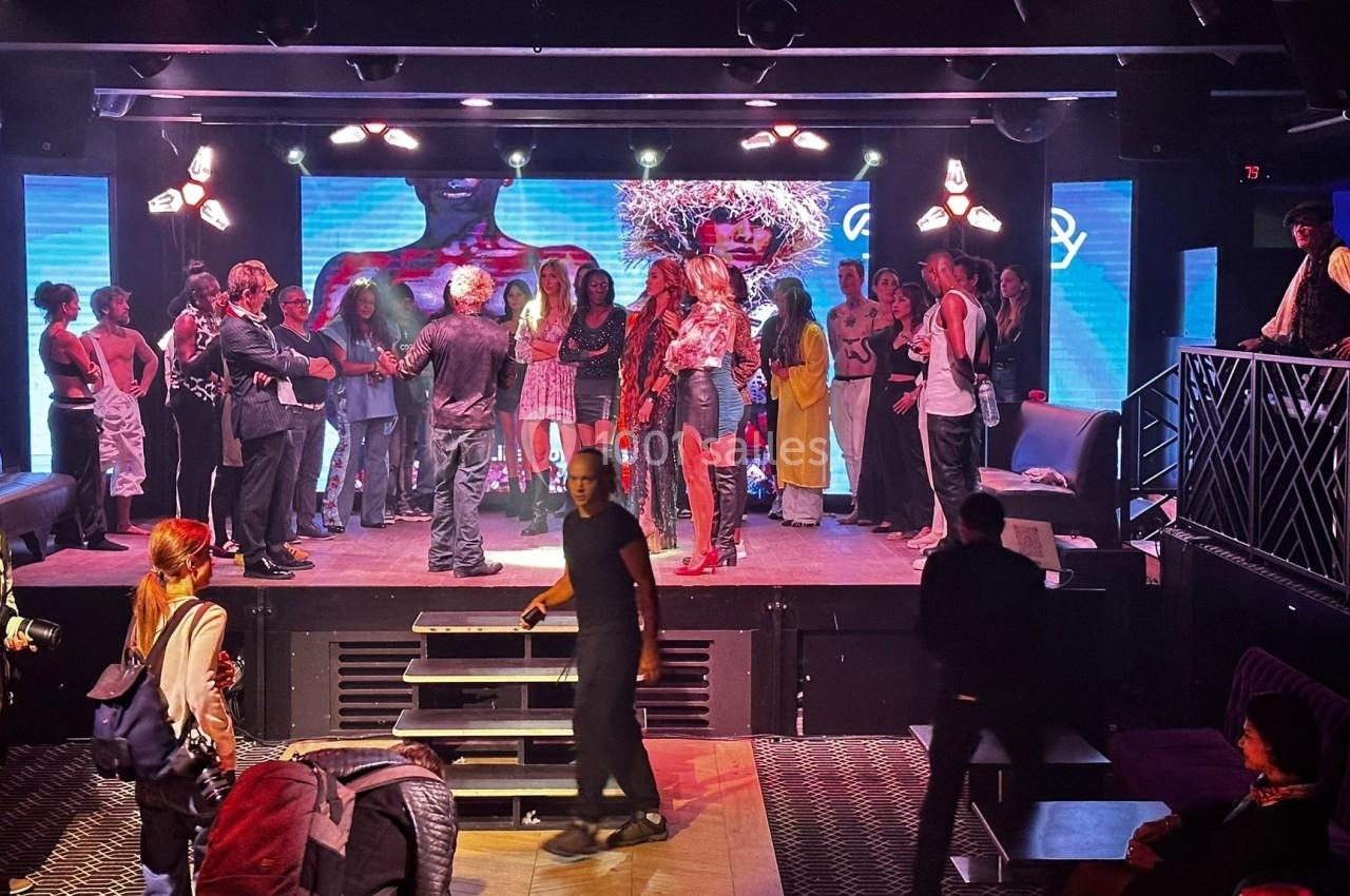 Un groupe de personnes rassemblé sur une scène et autour, dans un espace intérieur avec éclairage coloré.