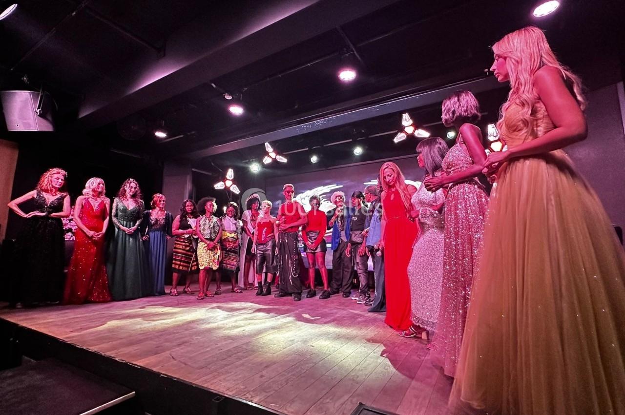 Un groupe de personnes en tenue de soirée est rassemblé sur une scène éclairée dans une salle sombre.