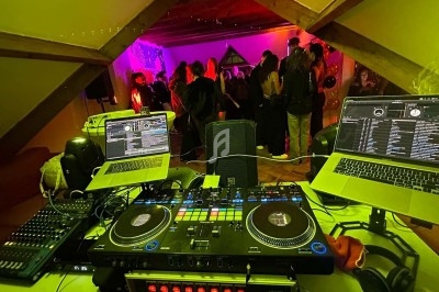 Salle obscure avec éclairage violet et vert, fumée diffuse, table dressée sur la gauche et rideaux brillants en arrière-plan.