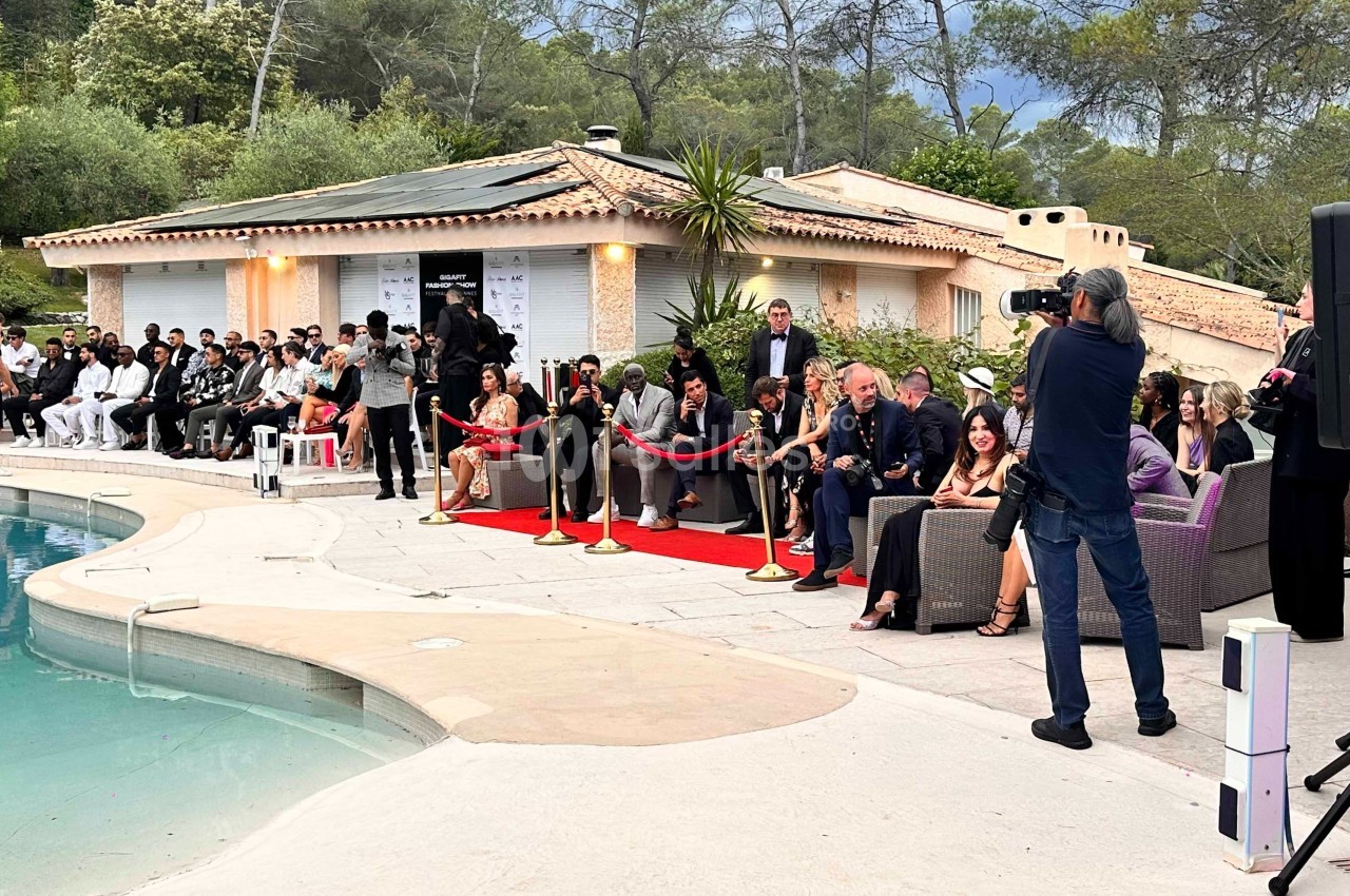 Un photographe capture un événement en plein air près d'une piscine, avec des invités assis et un tapis rouge.