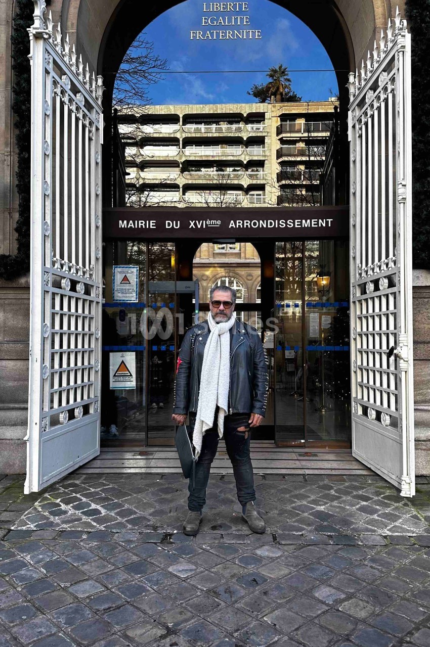 Homme debout devant l'entrée de la mairie du 16e arrondissement de Paris, avec des grilles ouvertes et une façade vitrée.