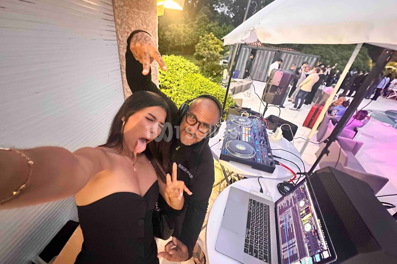 Une femme et un DJ posent joyeusement près d'une table de mixage lors d'un événement en extérieur.