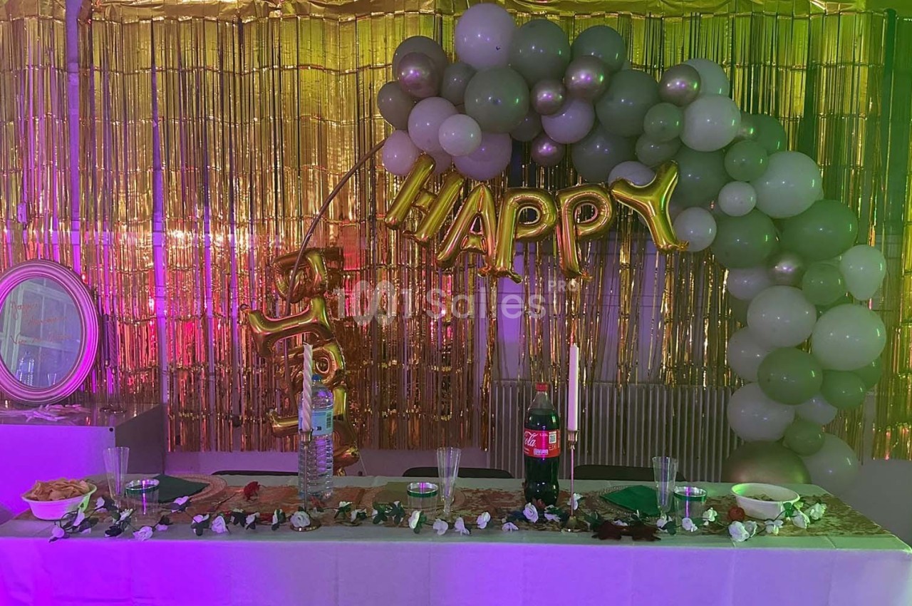 Décoration de fête avec ballons verts et dorés, guirlande ’Happy’, table dressée avec boissons et snacks.