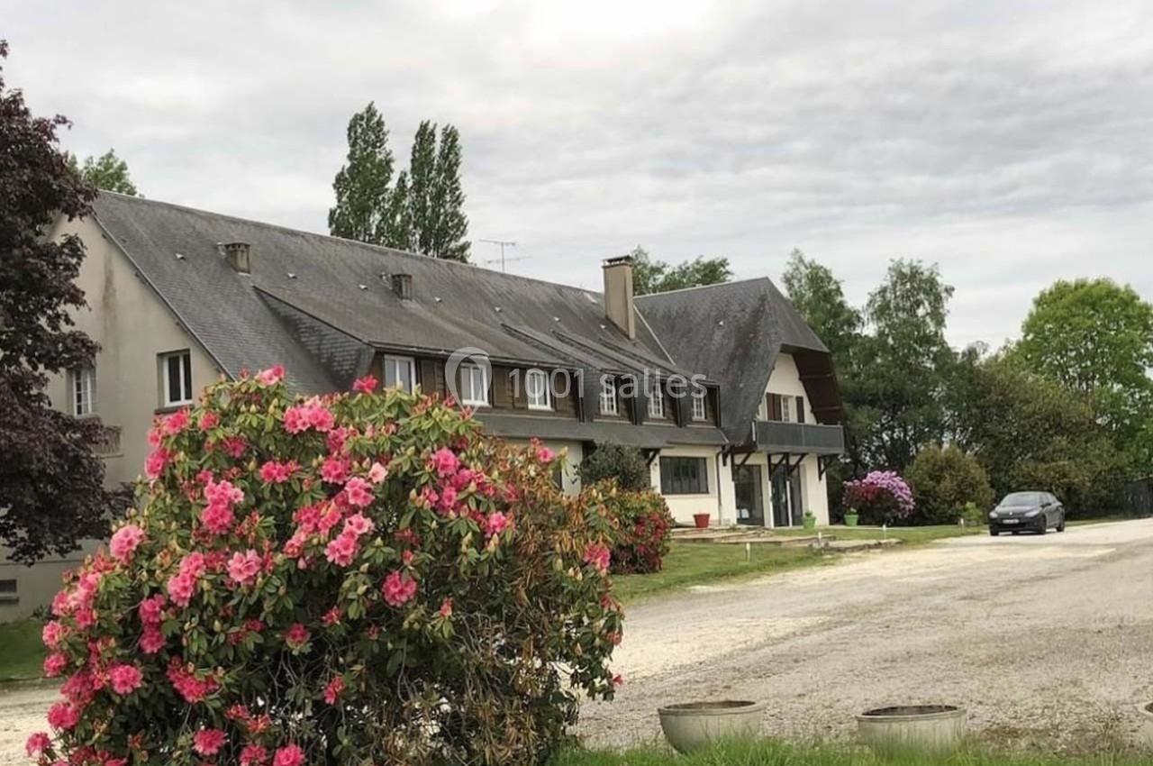 Grande maison en pierre avec toit en ardoise, entourée de buissons fleuris et d'une allée gravillonnée.