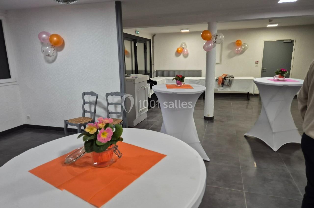 Salle décorée avec des ballons et des tables hautes ornées de nappes blanches et de bouquets de fleurs colorées.