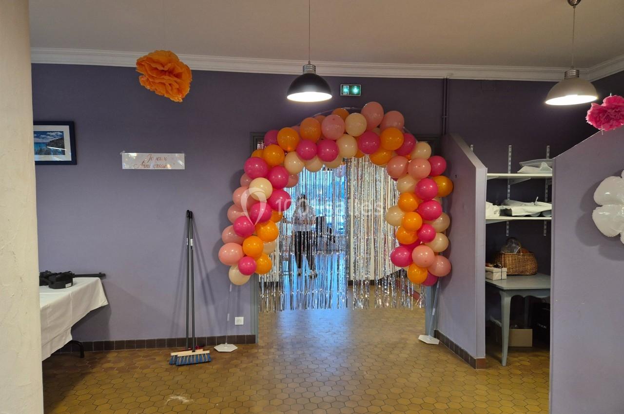 Arche de ballons roses et oranges décorant l'entrée d'une pièce avec un rideau scintillant en fond.